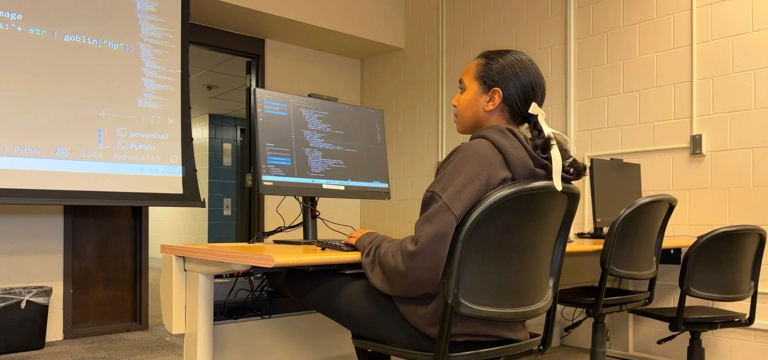 student sitting at a computer while writing code