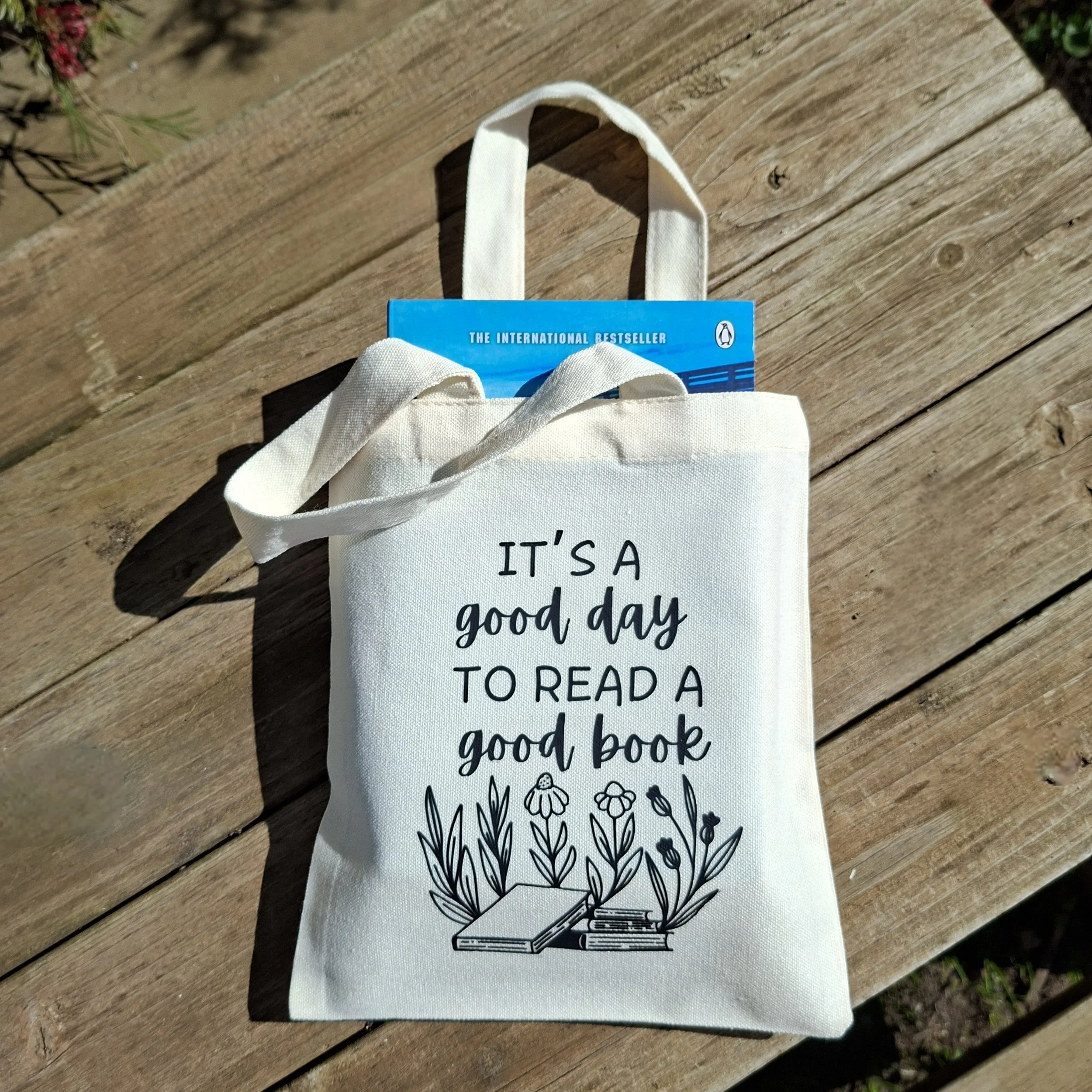 A white tote bag with the quote 'It's a good day to read a good book' and a line drawing of open books surrounded by flowers.