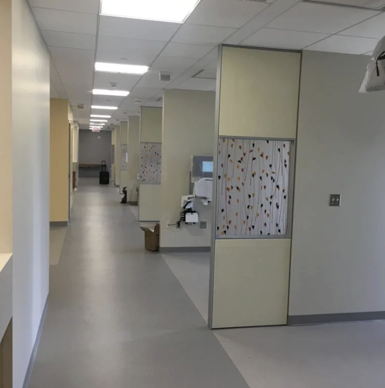 Empty hospital corridor with medical equipment and partitioned rooms.