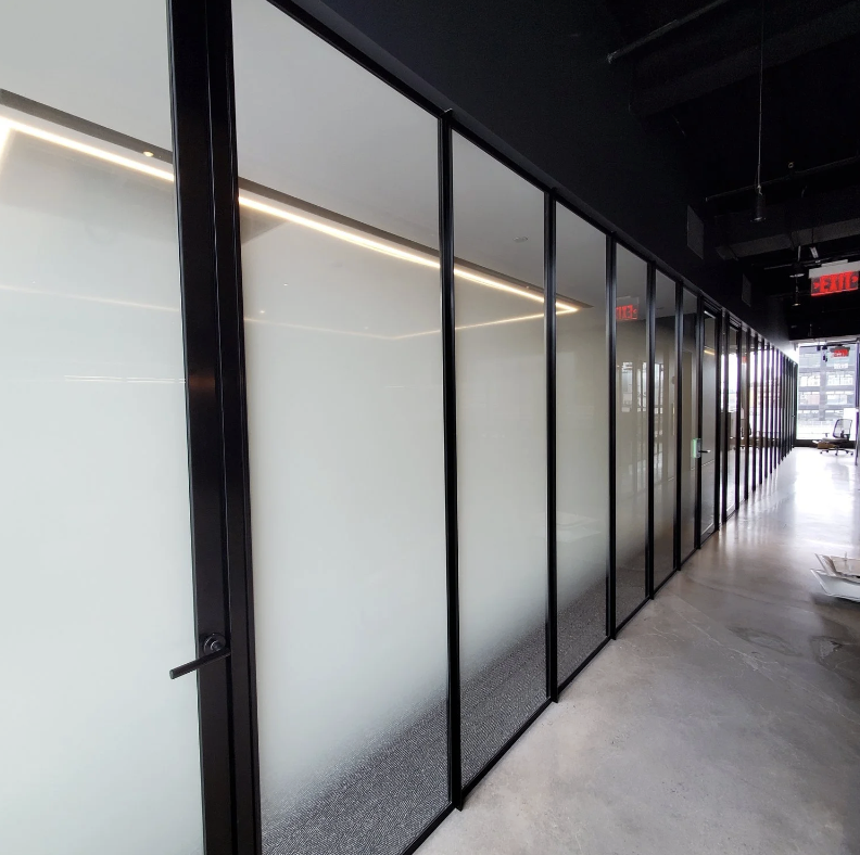 Modern office space with frosted glass partition walls and a corridor, with an illuminated ceiling and a visible exit sign.