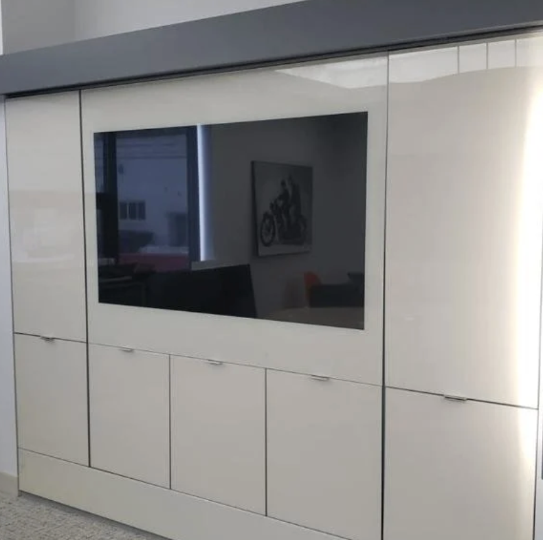 A modern office or reception area featuring a large, built-in white cabinet with a mirrored or TV screen in the middle reflecting a picture of a motorcycle.