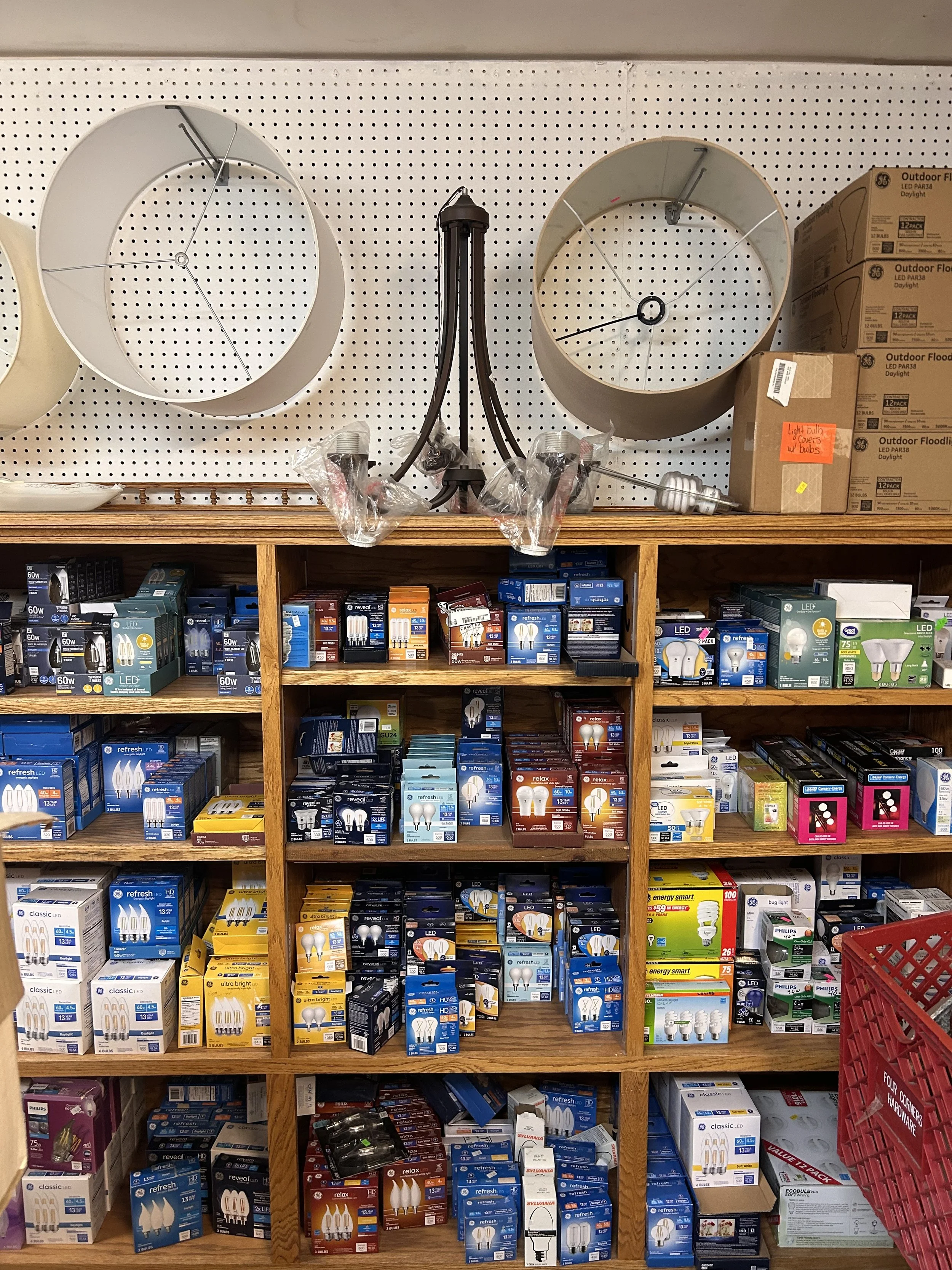 Shelves of new lightbulbs. Lampshades hanging on the wall above the shelves.