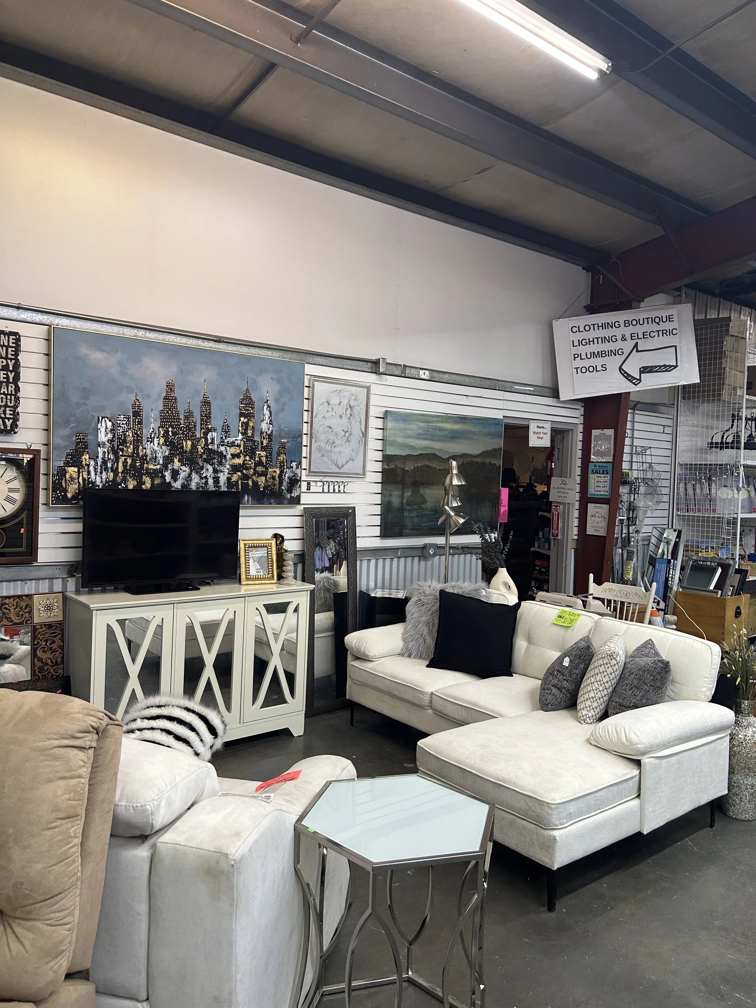 ReStore goods out on the floor. White sofa, white chair, side table, entertainment center, Tv, and wall art positioned to mimic a living room arrangement.