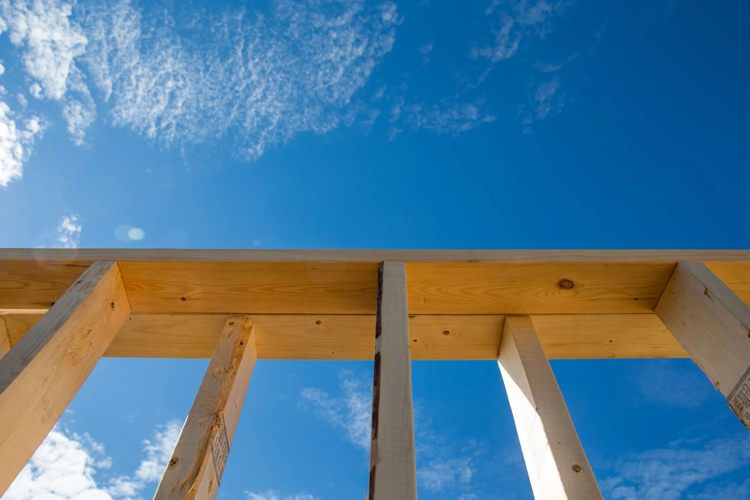 Wooden framing structure for a building under construction. The sky is blue with some white clouds.