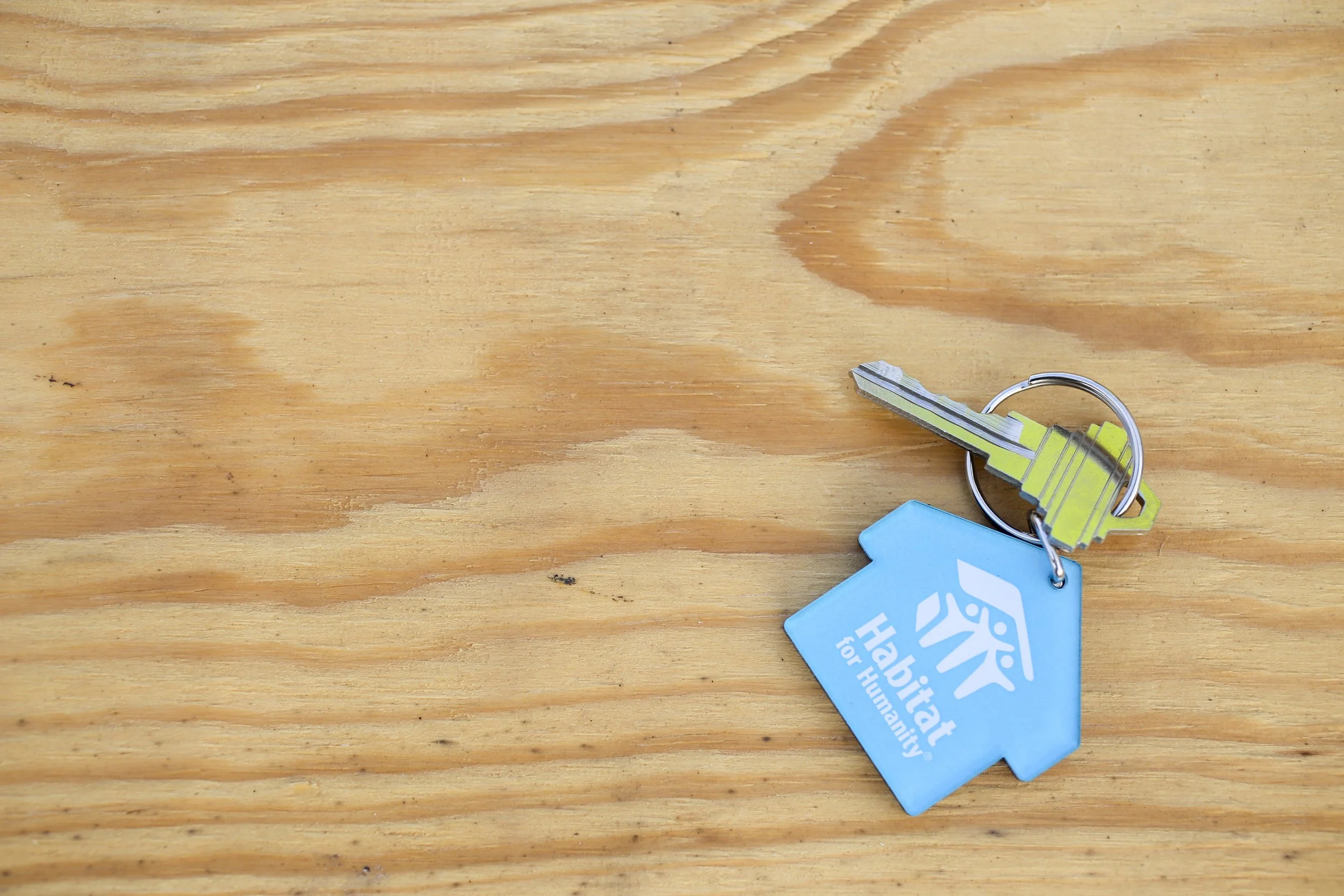 Wood table with a key laying on it with an attached keychain reading "Habitat for Humanity"
