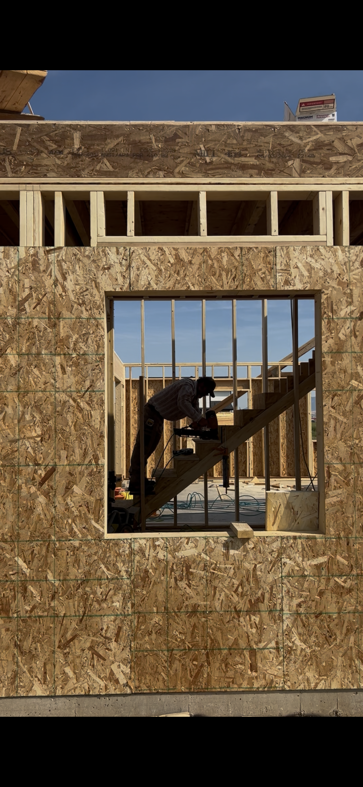 A man building stairs in a house shot through the framed window.