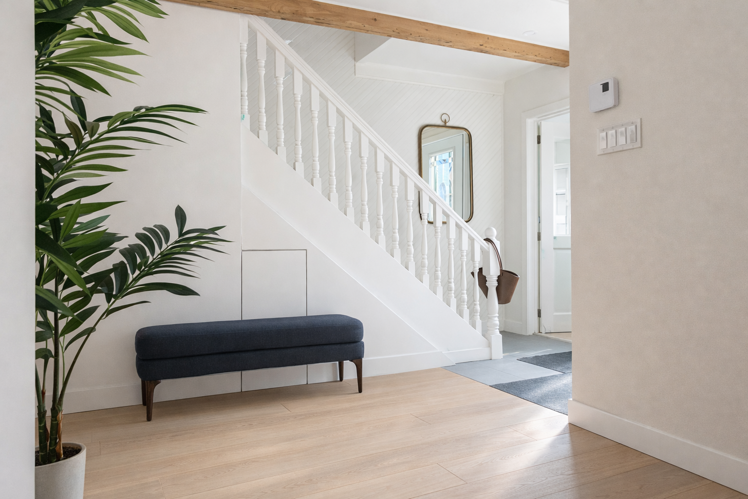 Entryway with a white staircase, a mirror, a brown bag hanging on the staircase, a dark blue bench, a green potted plant, and a door in the background.