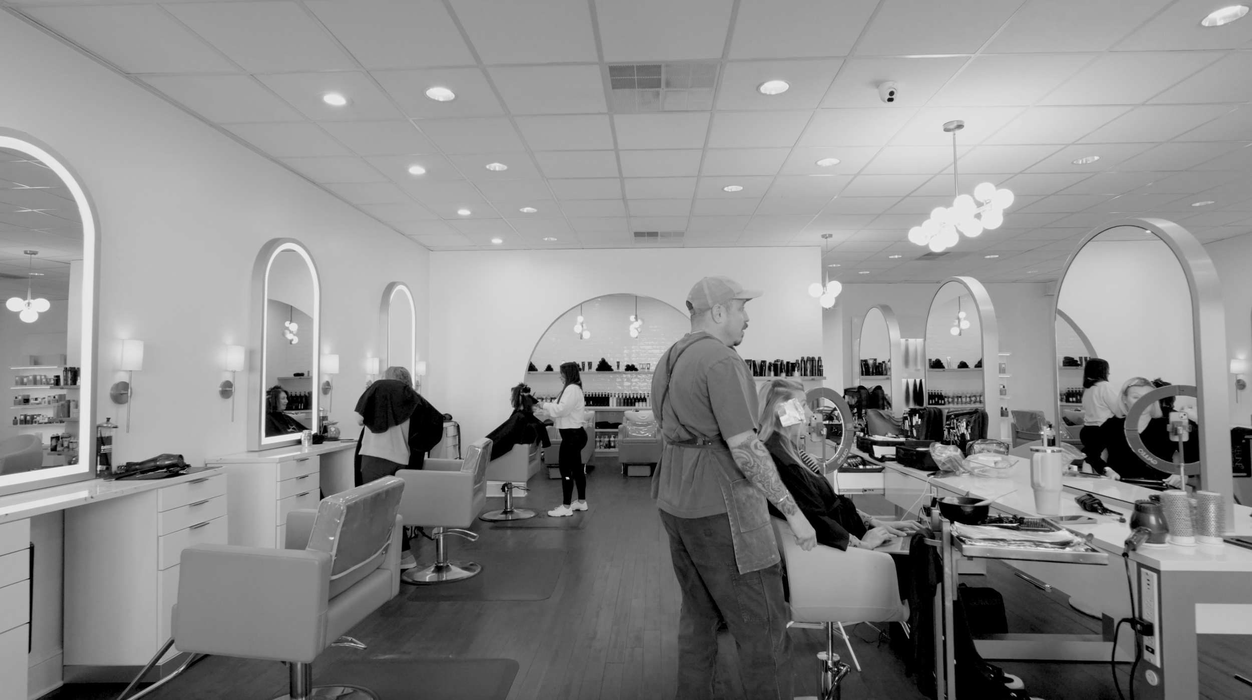 A modern hair salon with several clients getting hair treatments and haircuts, hairdressing stations with mirrors and salon equipment, and barber chairs.