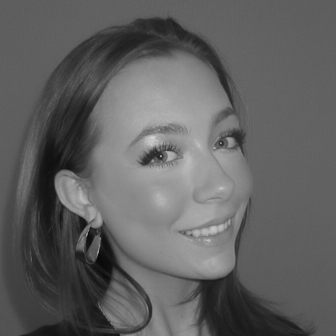 A black and white portrait of a young woman smiling, with shoulder-length hair, wearing large hoop earrings and makeup.