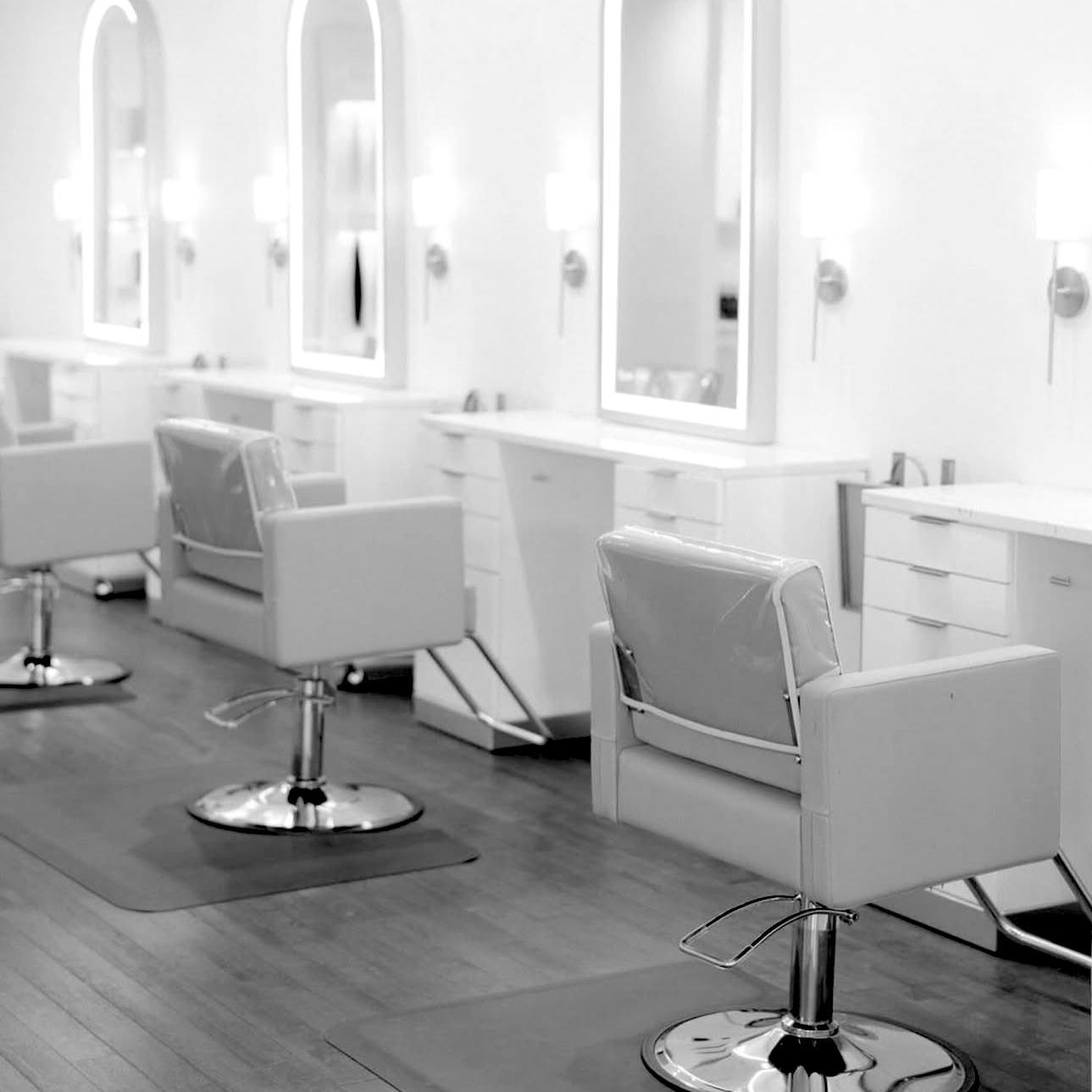Empty salon with styling chairs, mirrors, and wooden flooring.