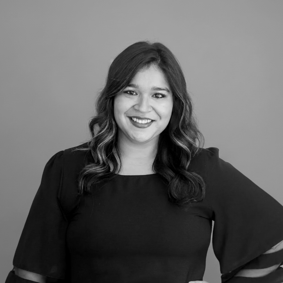 Black and white portrait of a smiling woman with wavy hair, wearing a dark top with puffed sleeves, standing against a plain background.