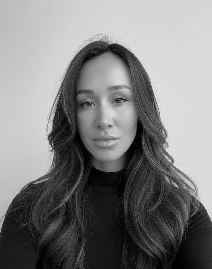 Black and white portrait of a woman with long, wavy hair wearing a dark top, looking at the camera with a neutral expression.