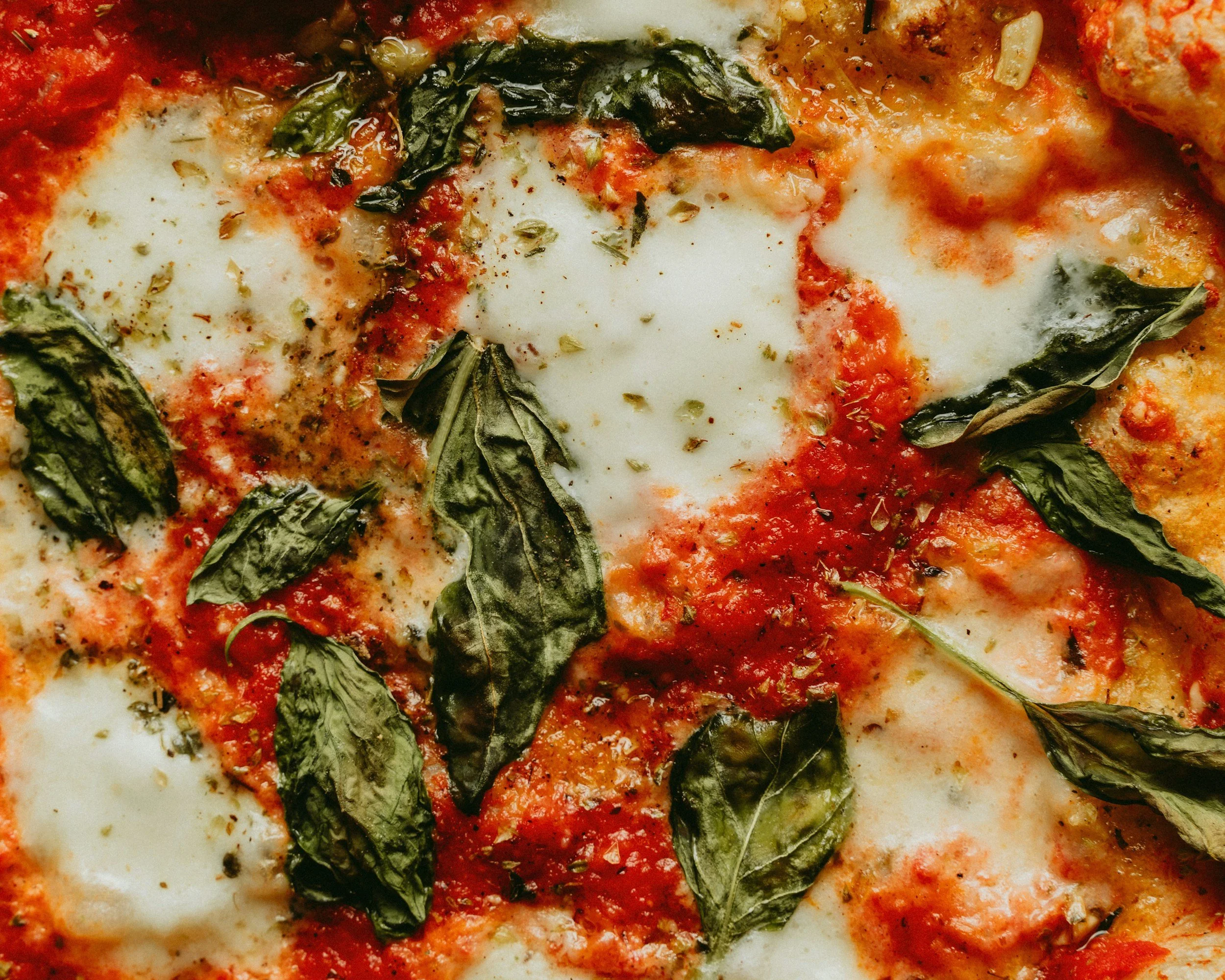 Close-up of a pizza topped with fresh basil leaves, melted cheese, tomato sauce, and herbs.