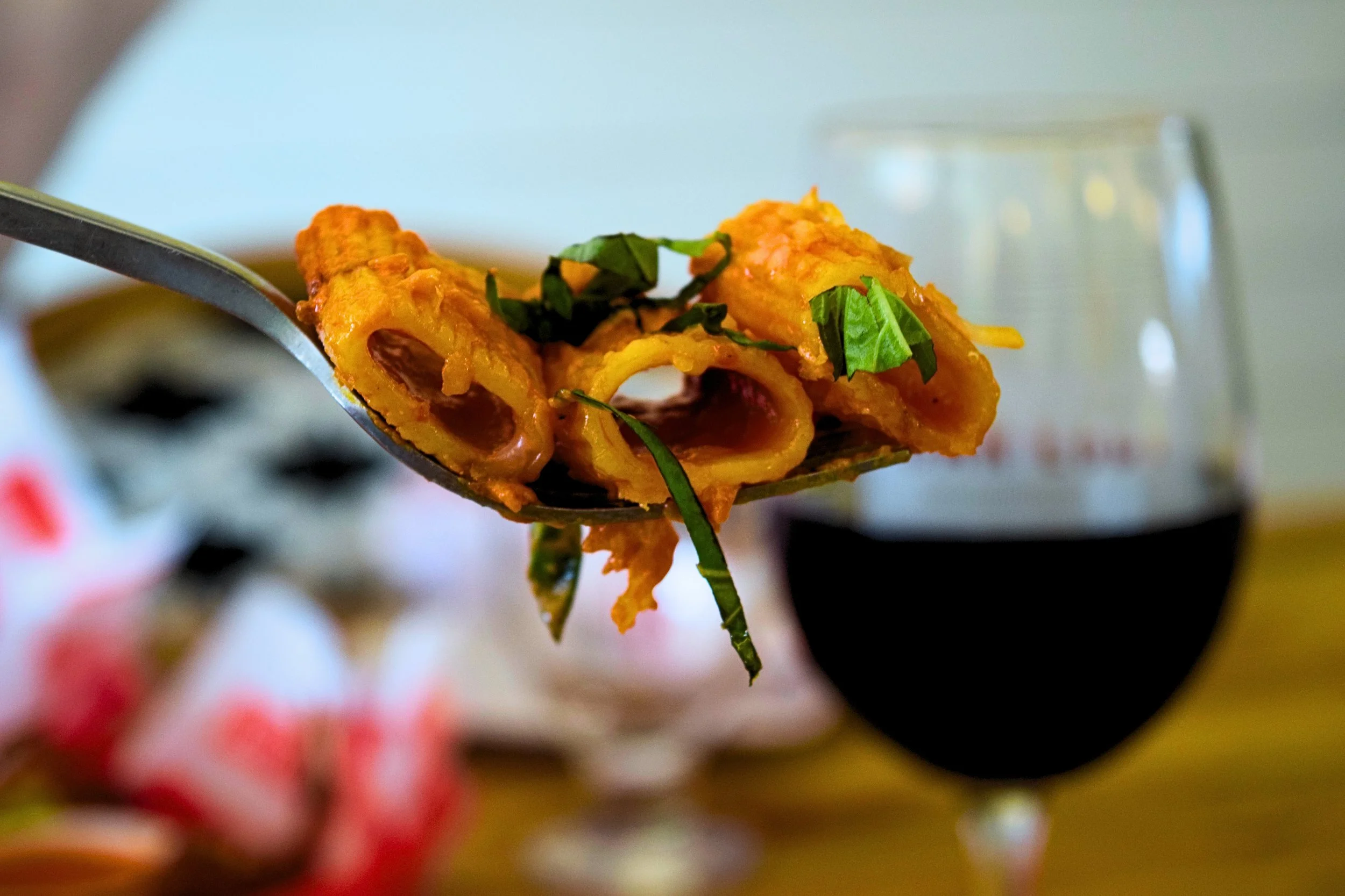 Close-up of a spoonful of Indian curry with vegetables, garnished with chopped green herbs, with a glass of red wine in the background.
