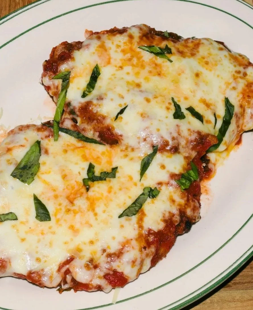 A plate of cheese and basil pizza with melted cheese, tomato sauce, green basil leaves, on a white dish with green lines.