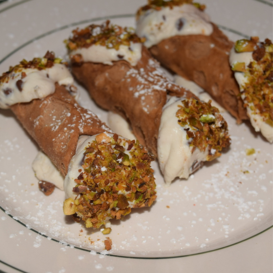 Four chocolate and vanilla ice cream roll cones with chopped pistachios on top, served on a white plate with powdered sugar.