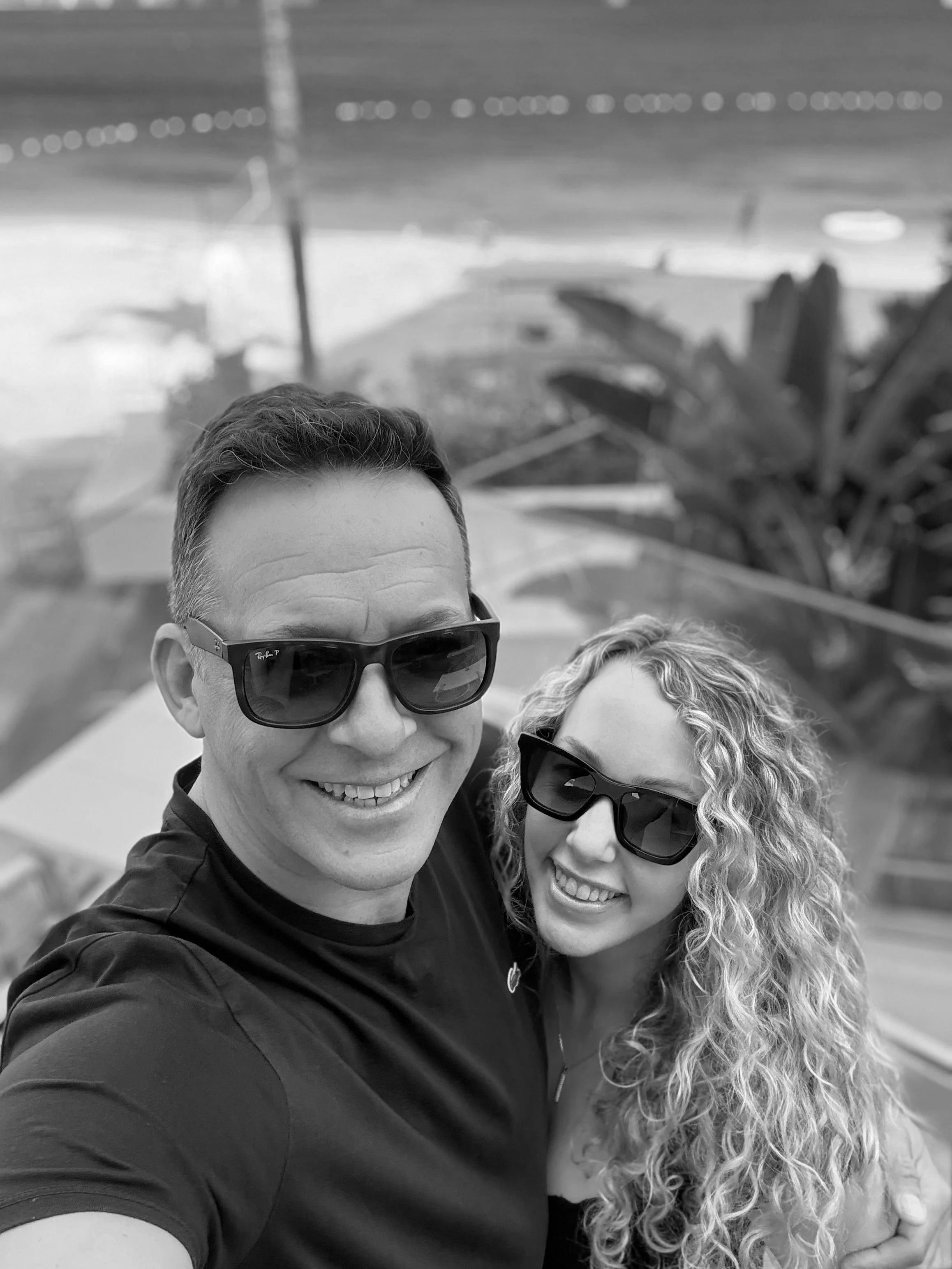 Un homme et une femme prennent un selfie en bord de mer. Ils portent tous deux des lunettes de soleil et sourient.