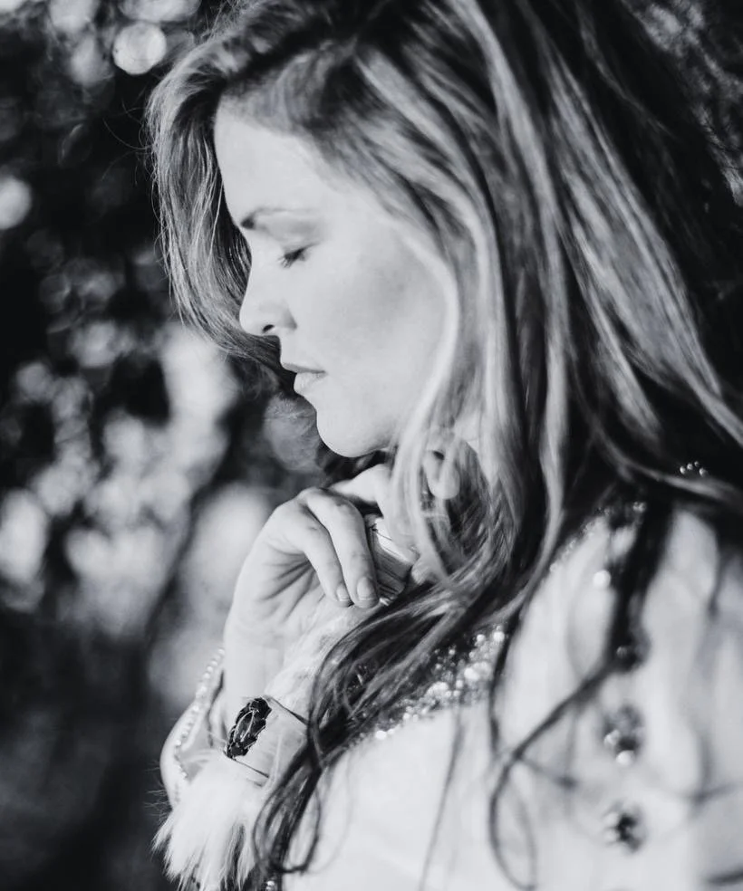 Black and white portrait of a woman with her eyes closed and her hand near her chin, with long wavy hair.