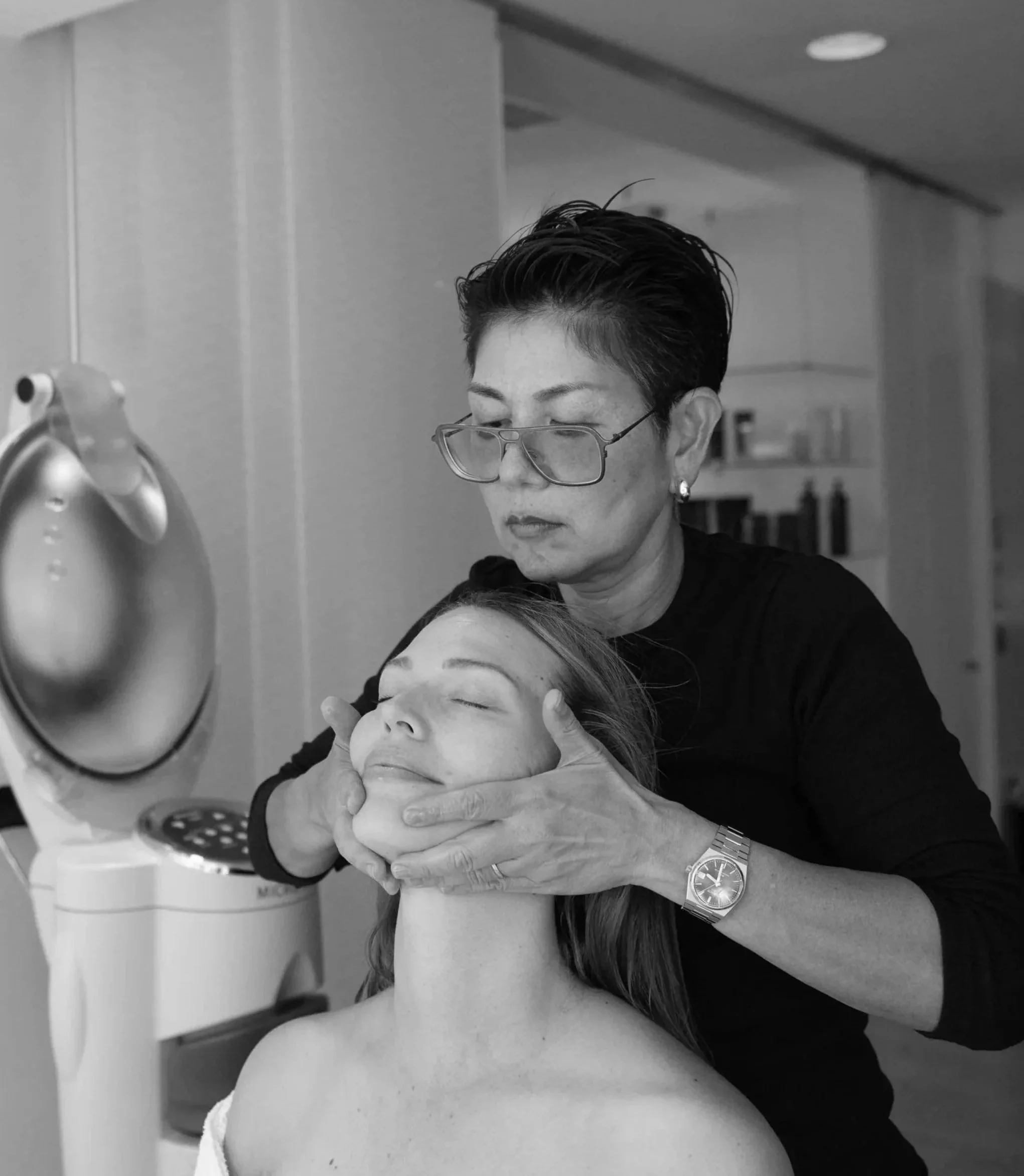 A woman with her eyes closed receiving a facial treatment from a beautician in a beauty salon.