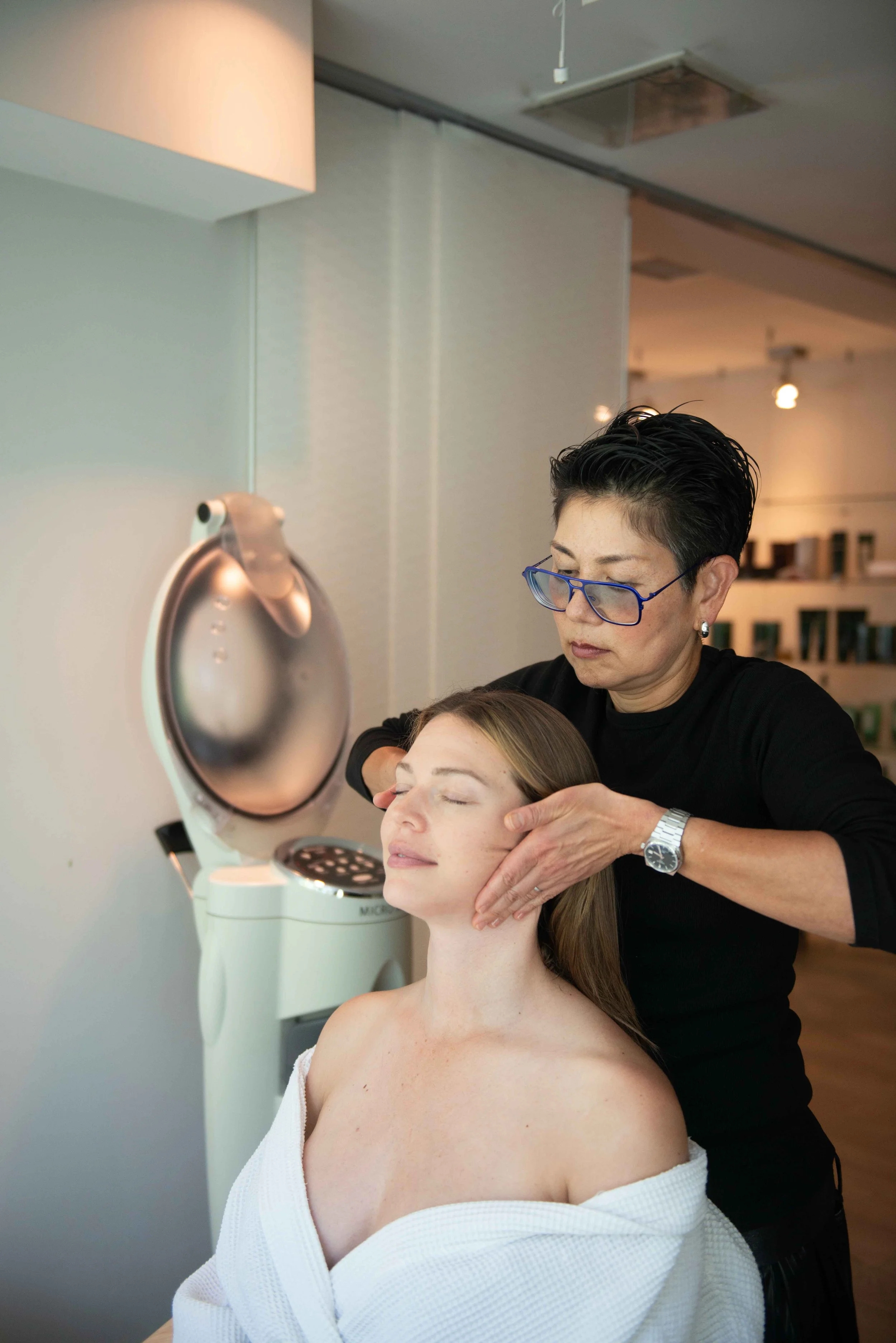 A woman with her eyes closed receiving a facial treatment from a beautician in a beauty salon.