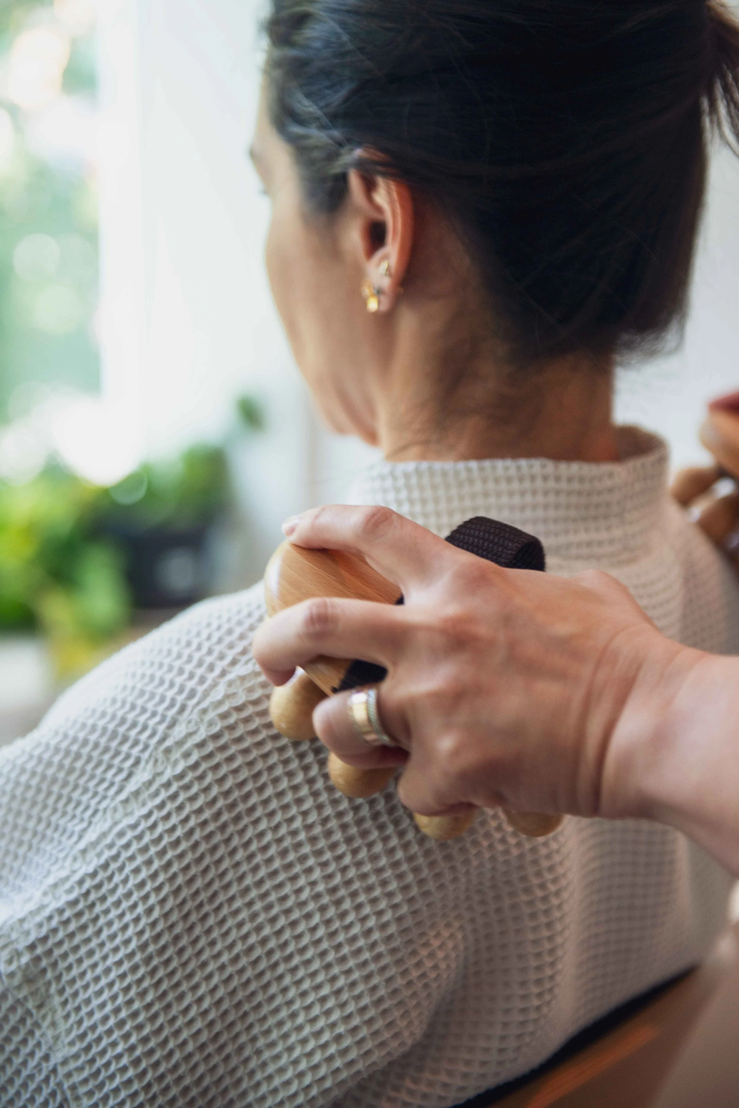 Person receiving a back massage with a wooden massage roller using both hands.