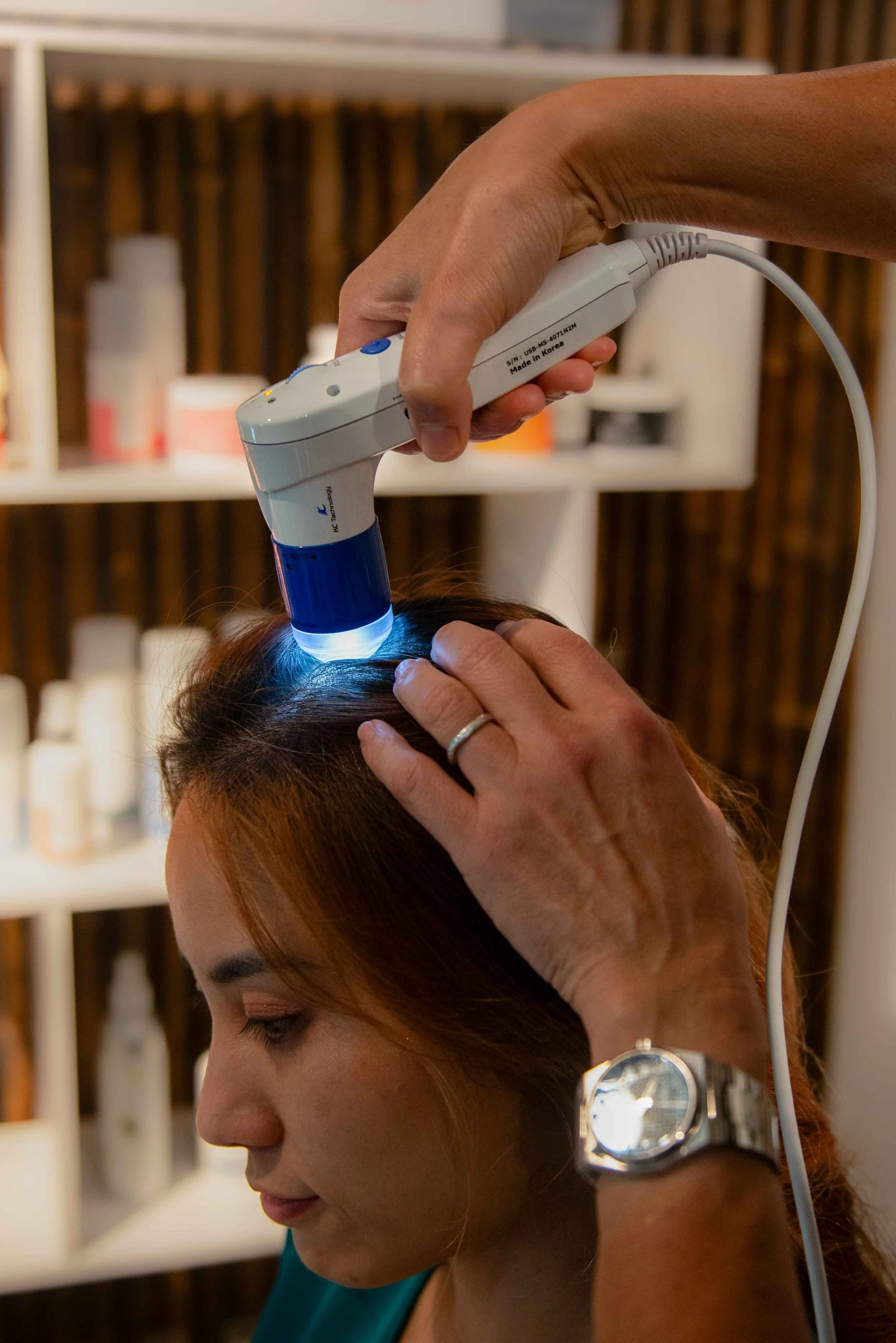 A person receiving a scalp treatment with a handheld device emitting blue light, held by a practitioner, in a salon setting.