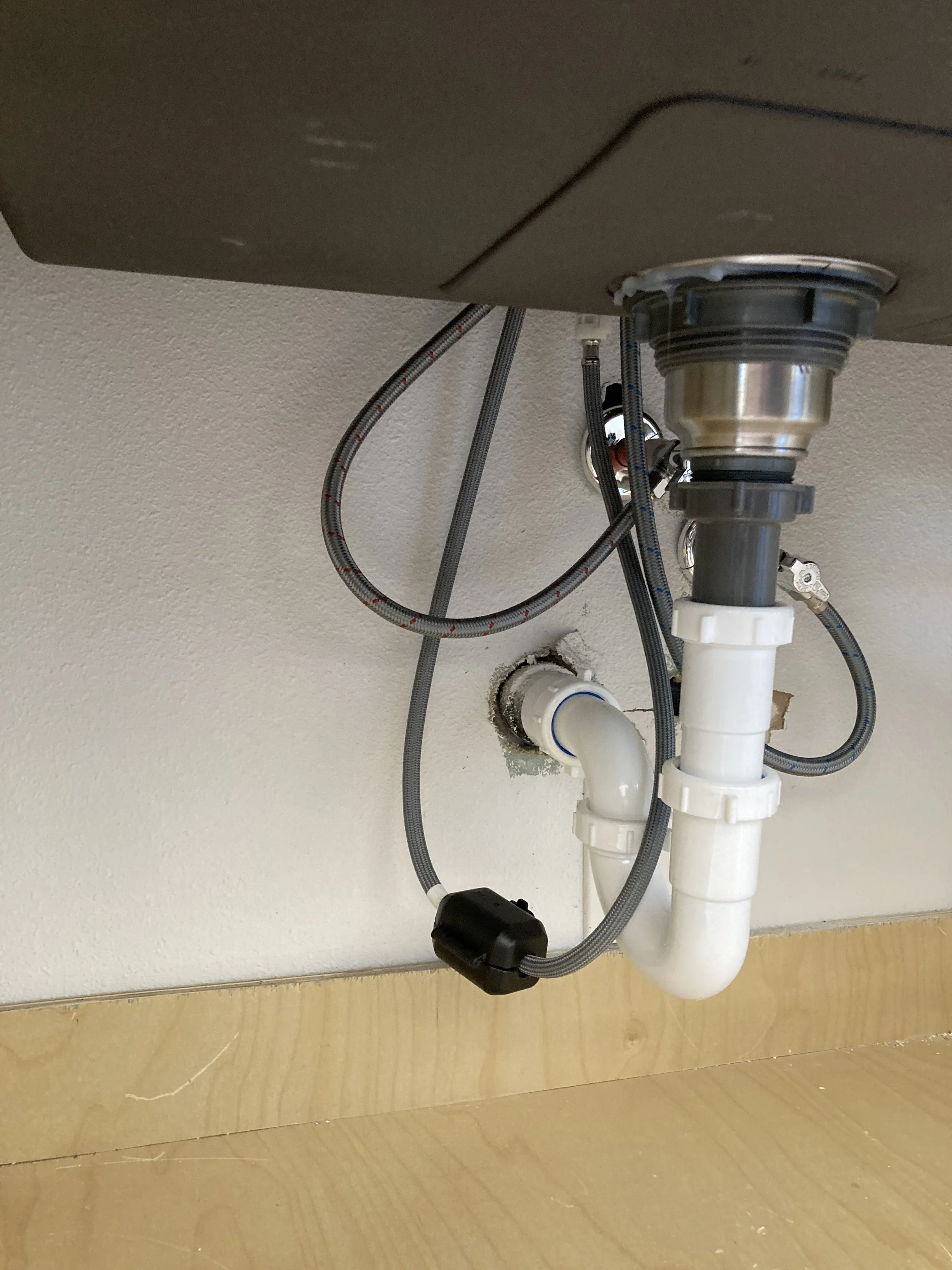 Under-sink plumbing with pipes, flexible braided hoses, and a drain with PVC pipes in a kitchen or bathroom.