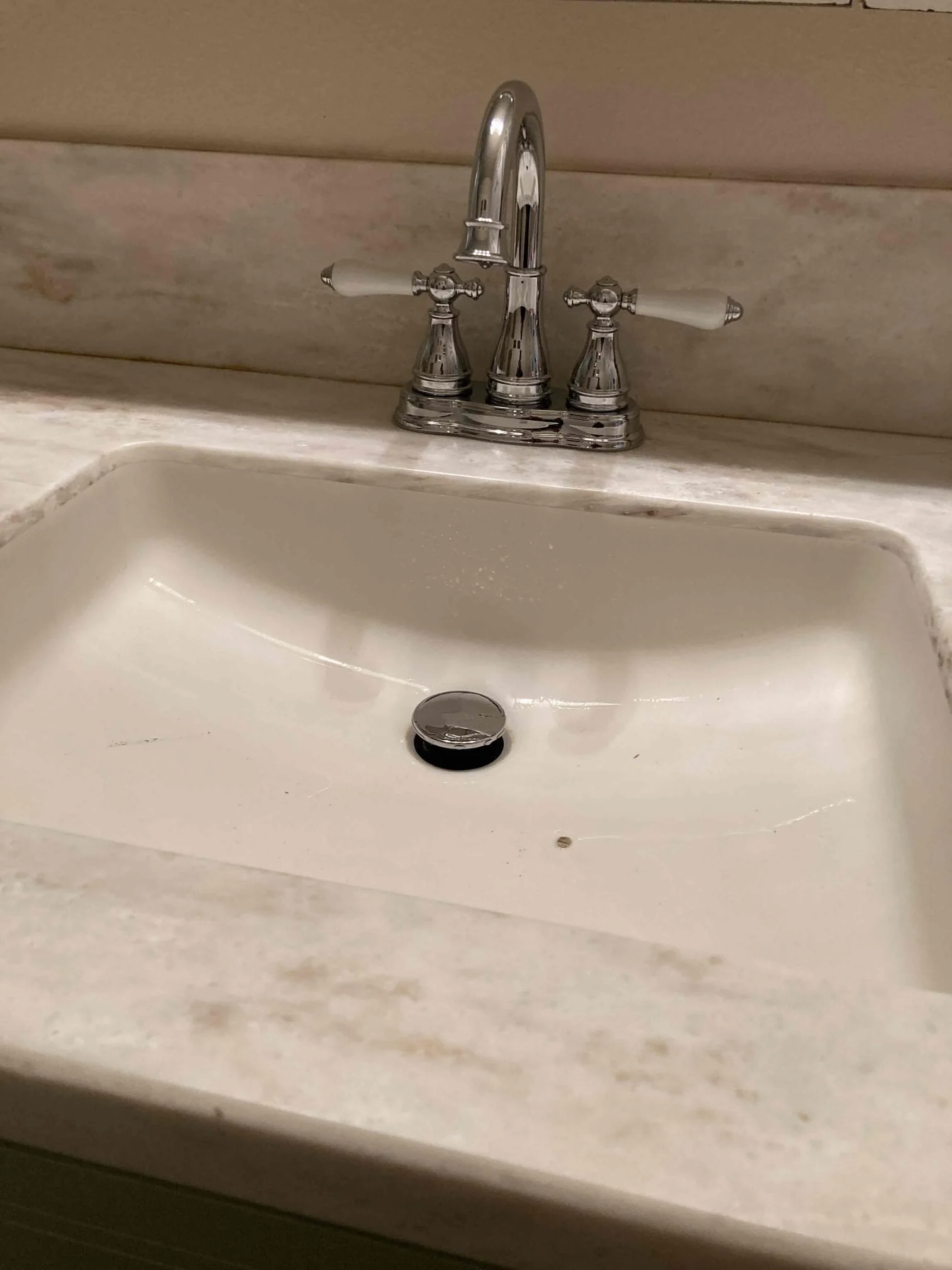 A bathroom sink with a chrome faucet and handles on a marble countertop.