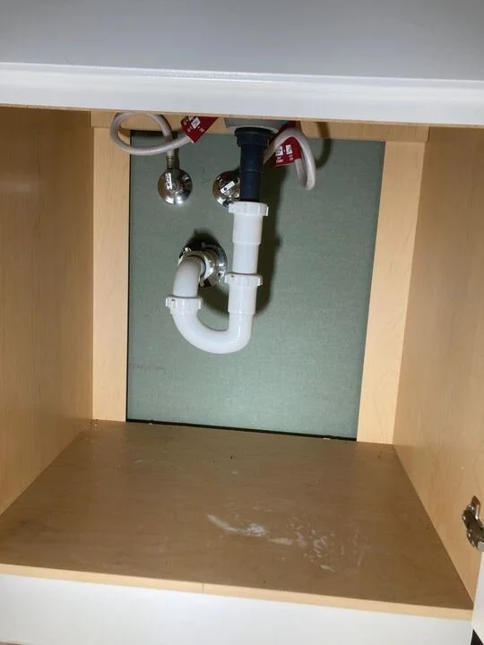 Underneath a kitchen sink showing plumbing pipes and shut-off valves.