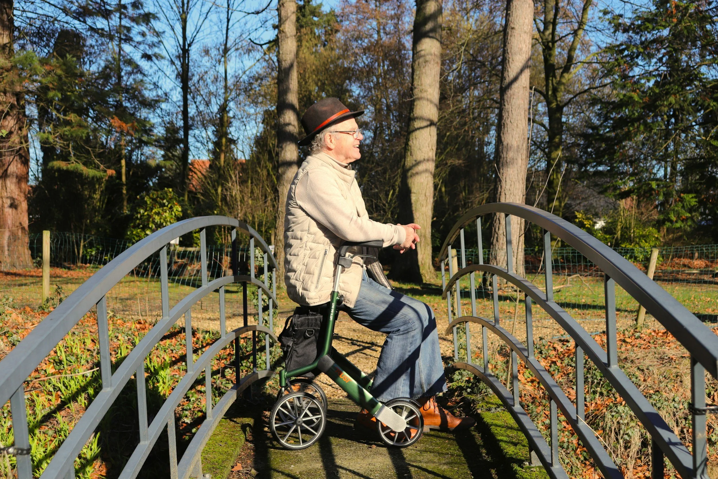 Older man smiling while in a wheelchair on a footbridge
