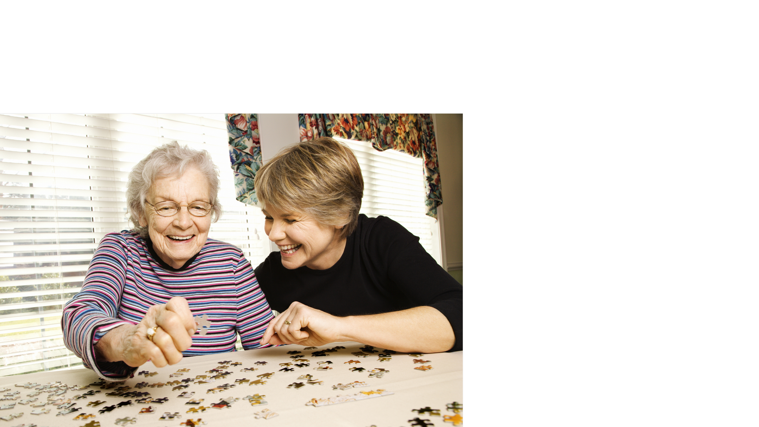 A younger woman helping an older woman play with puzzle pieces.
