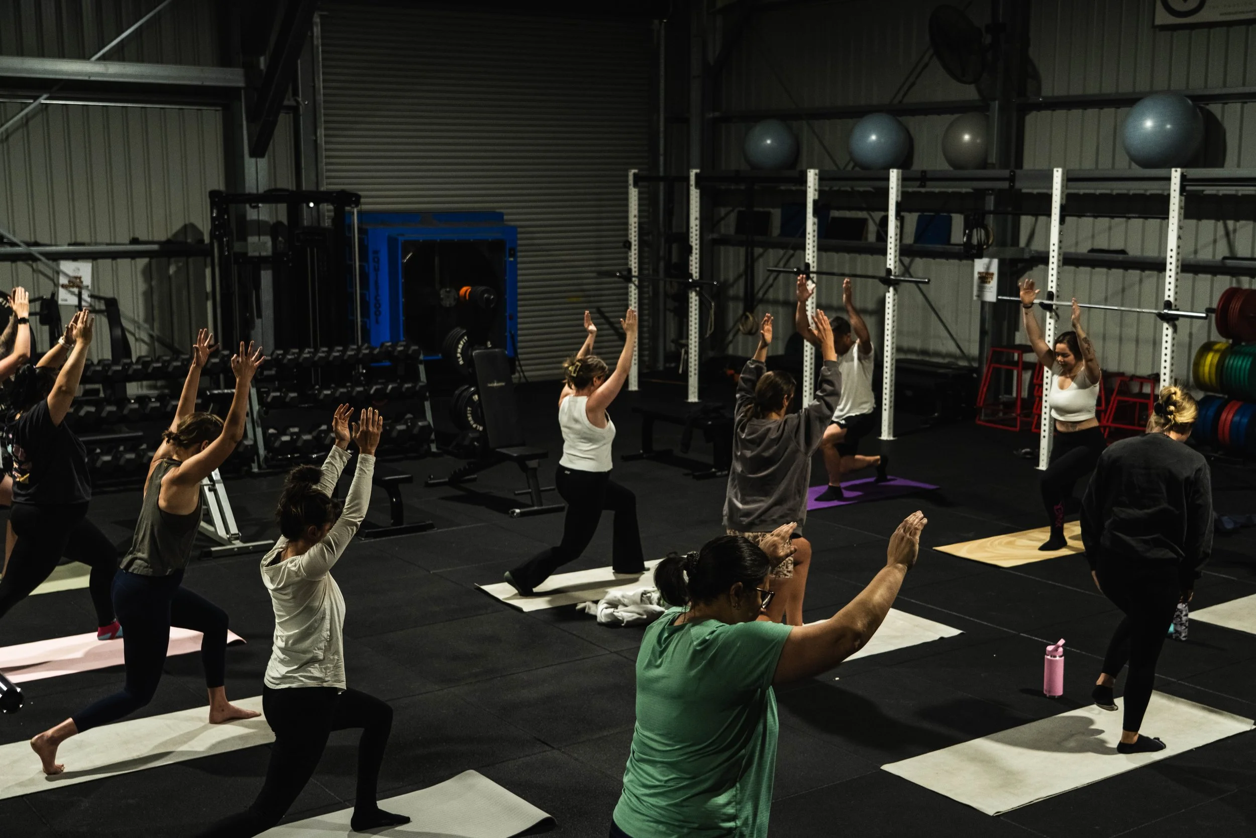 Group of people participating in a yoga class in a gym, practicing yoga poses on mats.