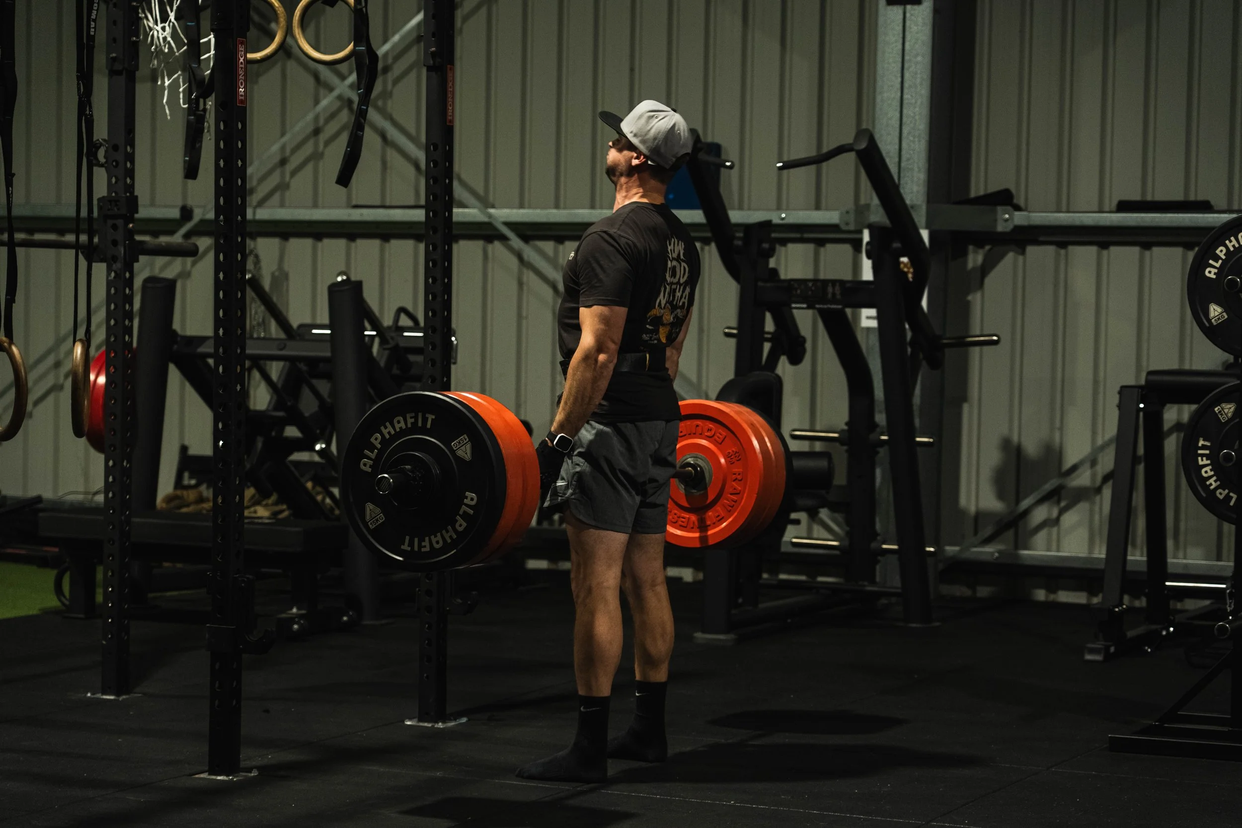 A man in a gym lifting a barbell loaded with orange and black weight plates.