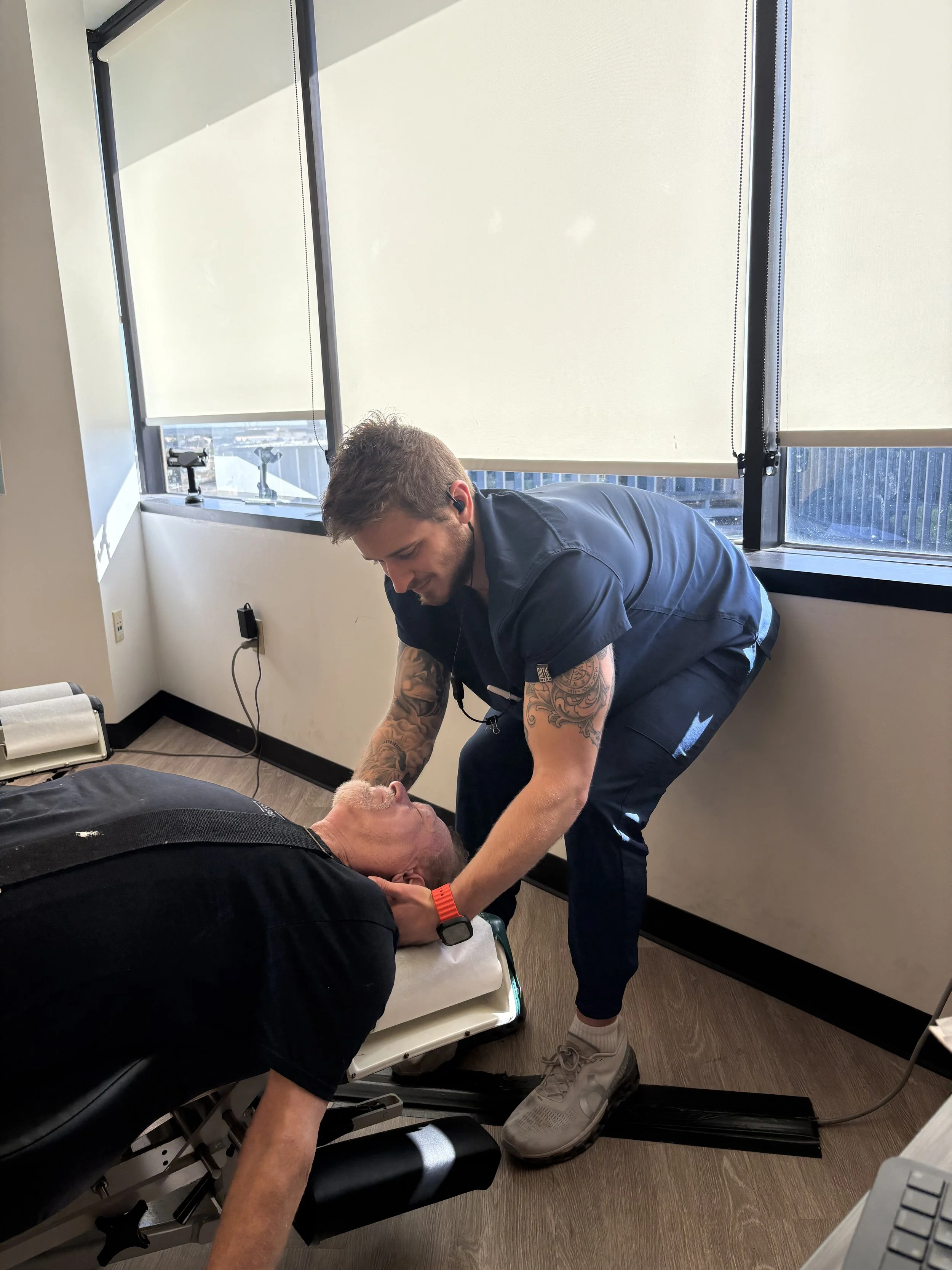 A healthcare professional performs a medical procedure on a patient lying on an examination table in a clinical setting.