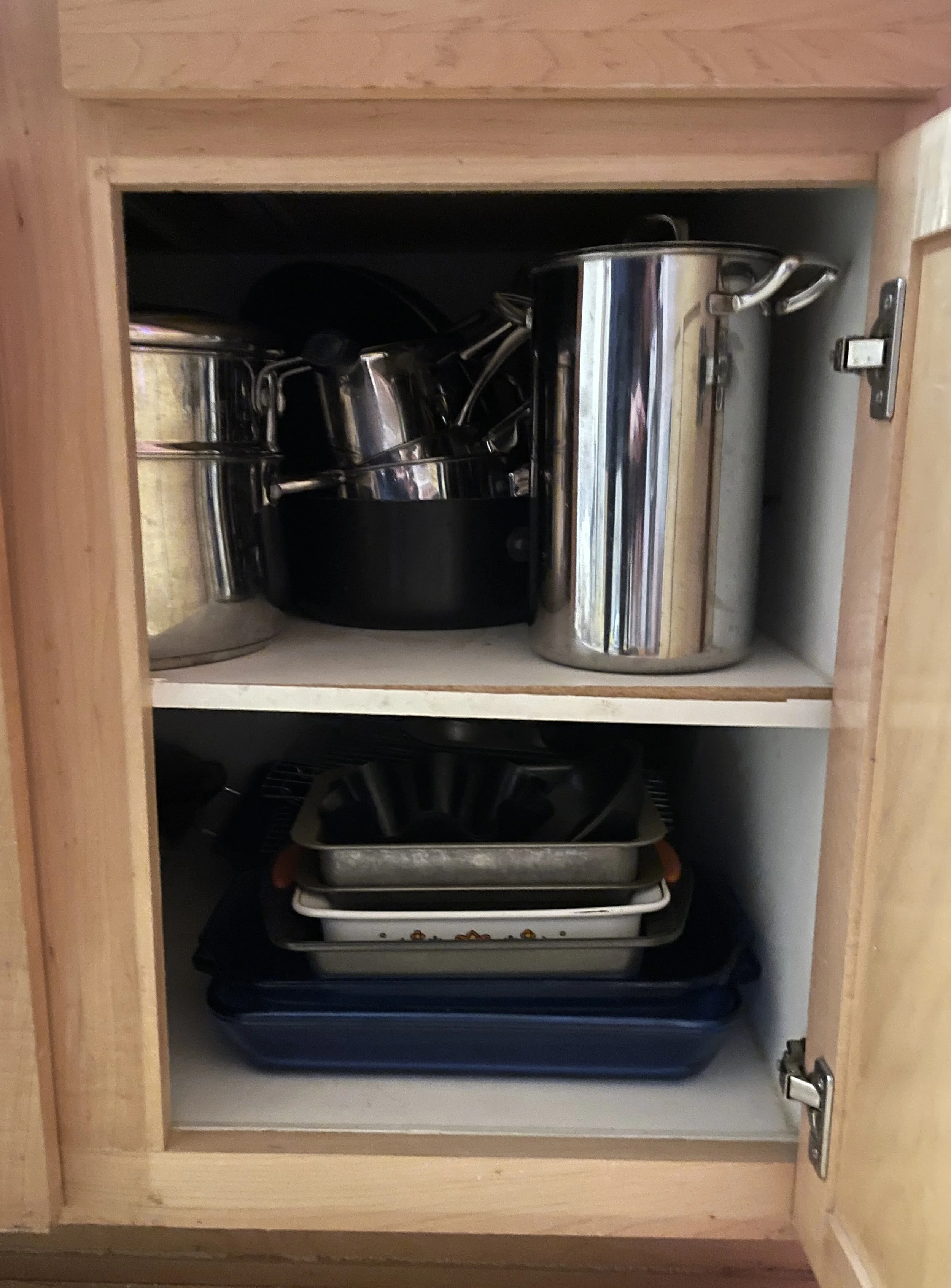Kitchen cabinet with metal pots, pans, and baking dishes inside.