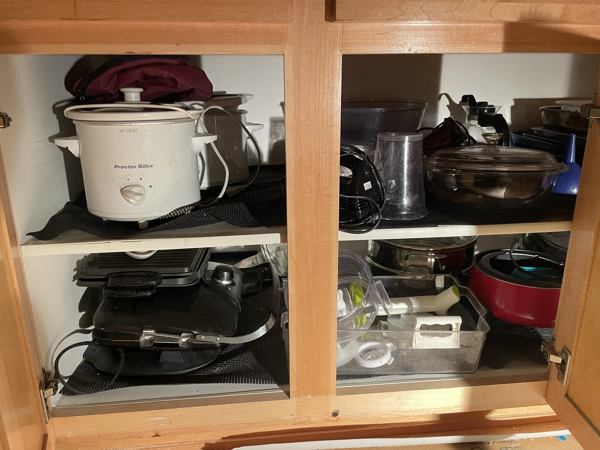 Open kitchen cabinet containing a rice cooker, various kitchen appliances, and kitchenware