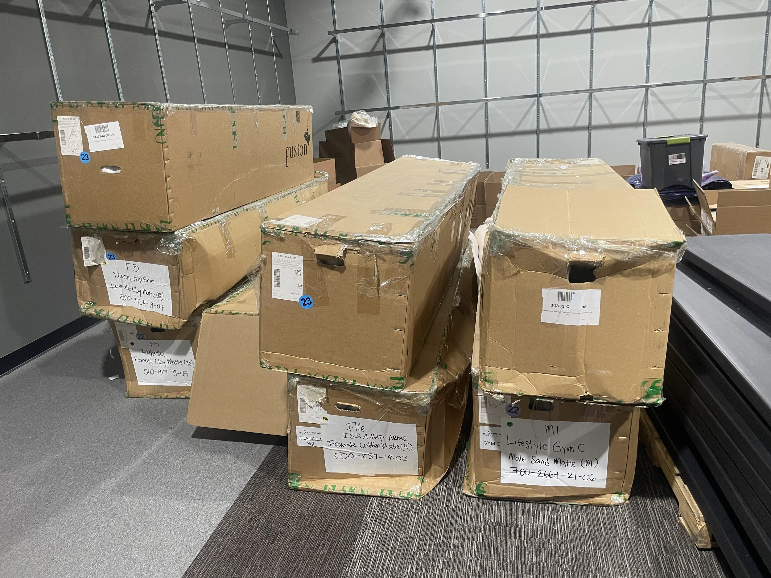 Stacked cardboard boxes in a storage room, some labeled with contents such as female matte and sand matte.
