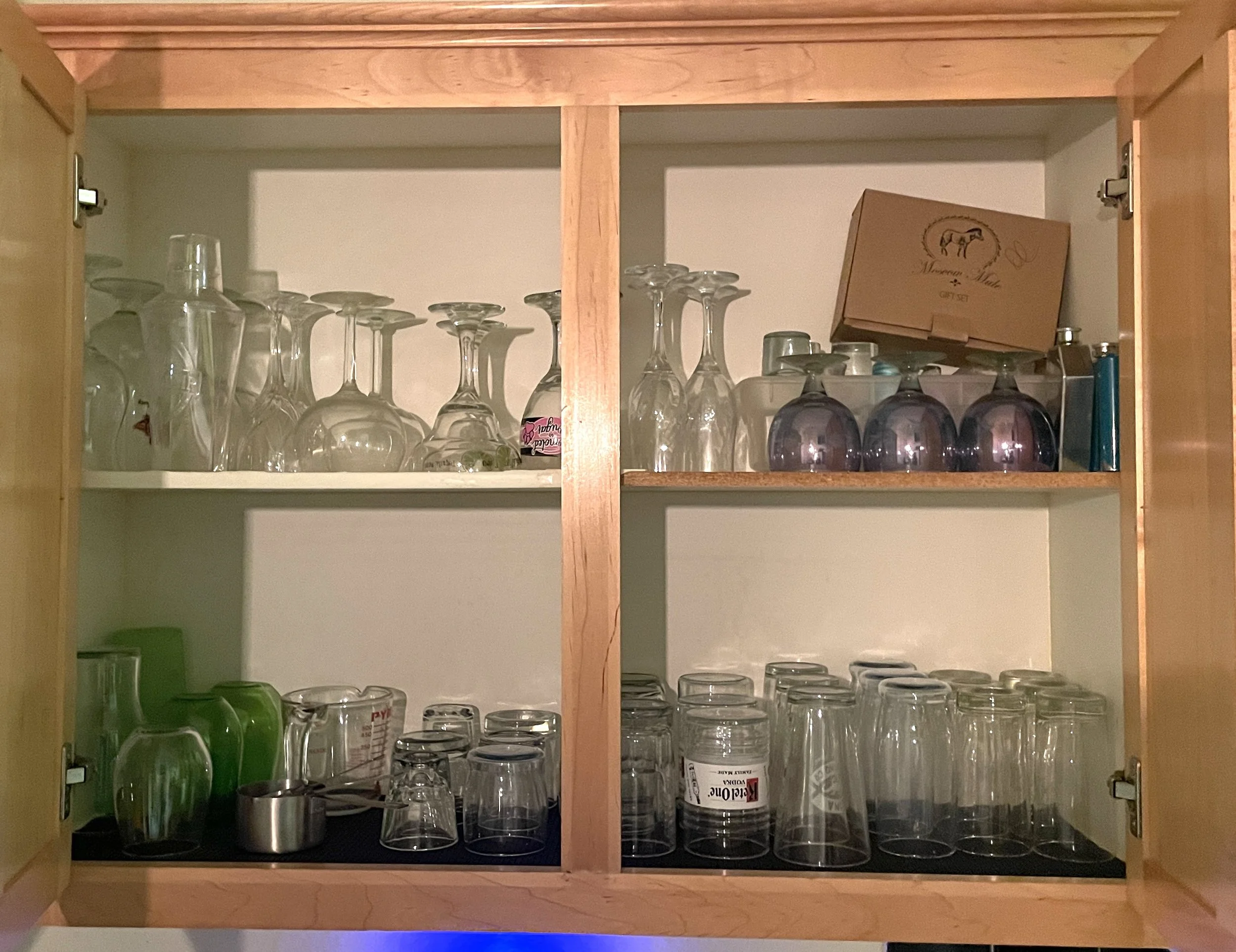 Inside of a wooden cabinet filled with upside-down wine glasses, cups, and containers.