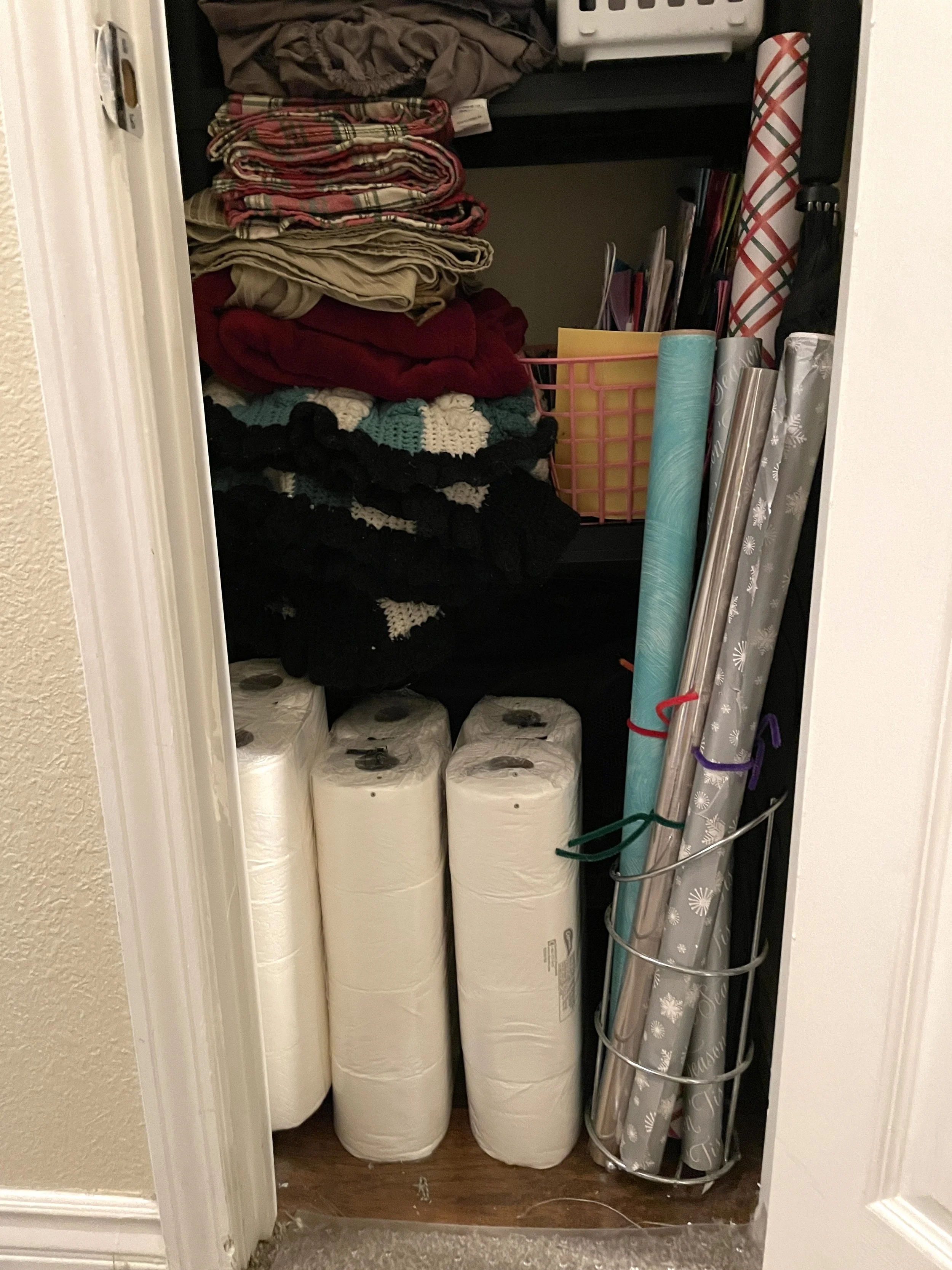 A closet with shelves holding folded clothes, rolls of wrapping paper, Christmas-themed wrapping paper, and containers of paper towels.