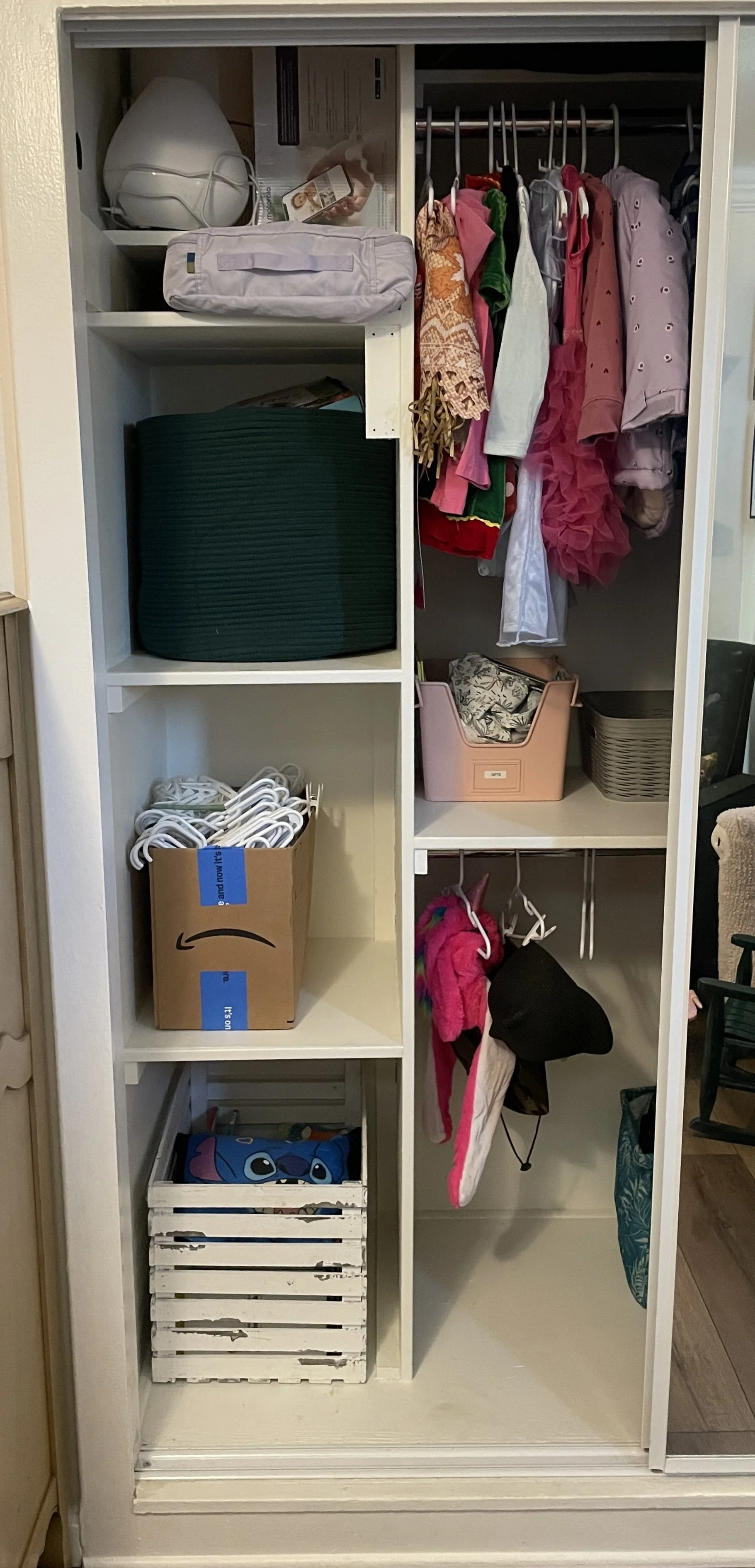 A closet with various organization containers and hanging clothes, including dresses, shirts, and jackets, with some toys and miscellaneous items.