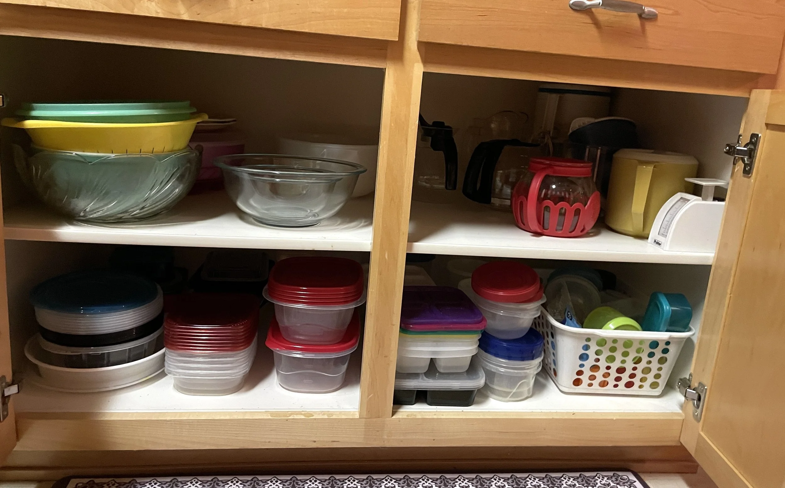 Open kitchen cabinet with glass bowls, plastic containers, and various kitchen items.