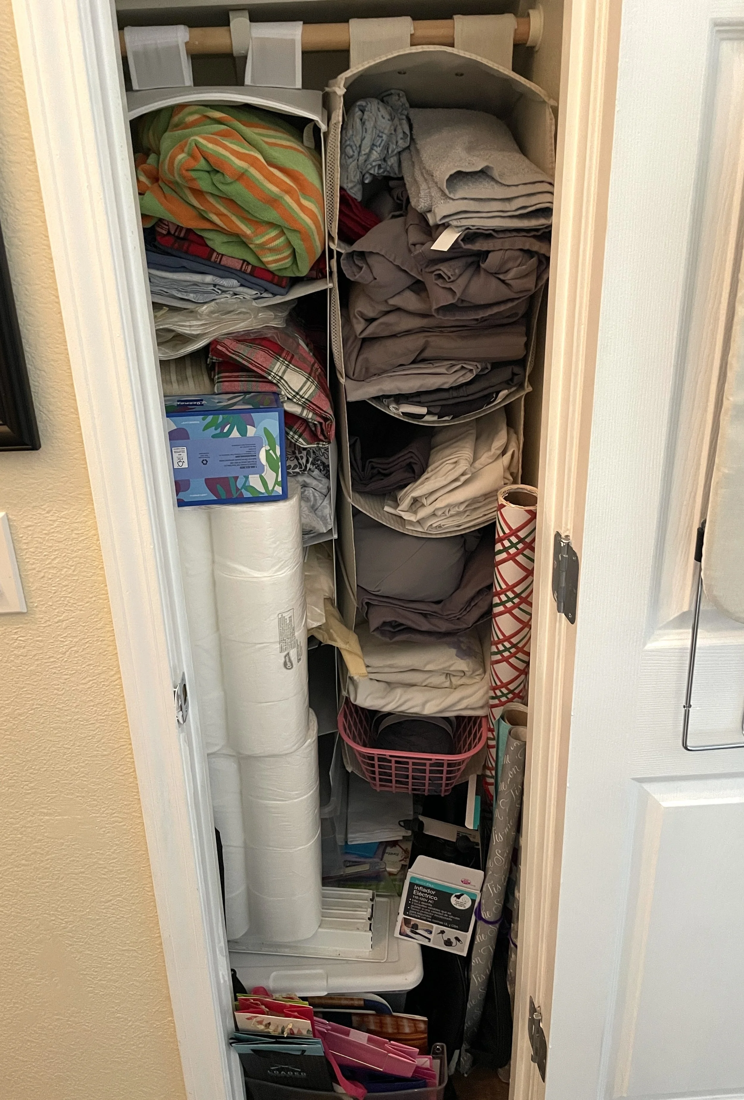 A small closet filled with neatly folded clothes, wrapping paper rolls, and storage containers.
