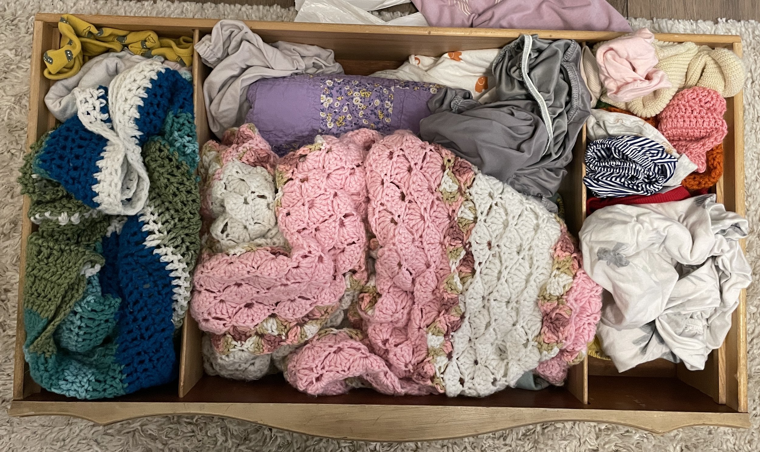 A wooden drawer filled with various colorful socks and hand-knit blankets.