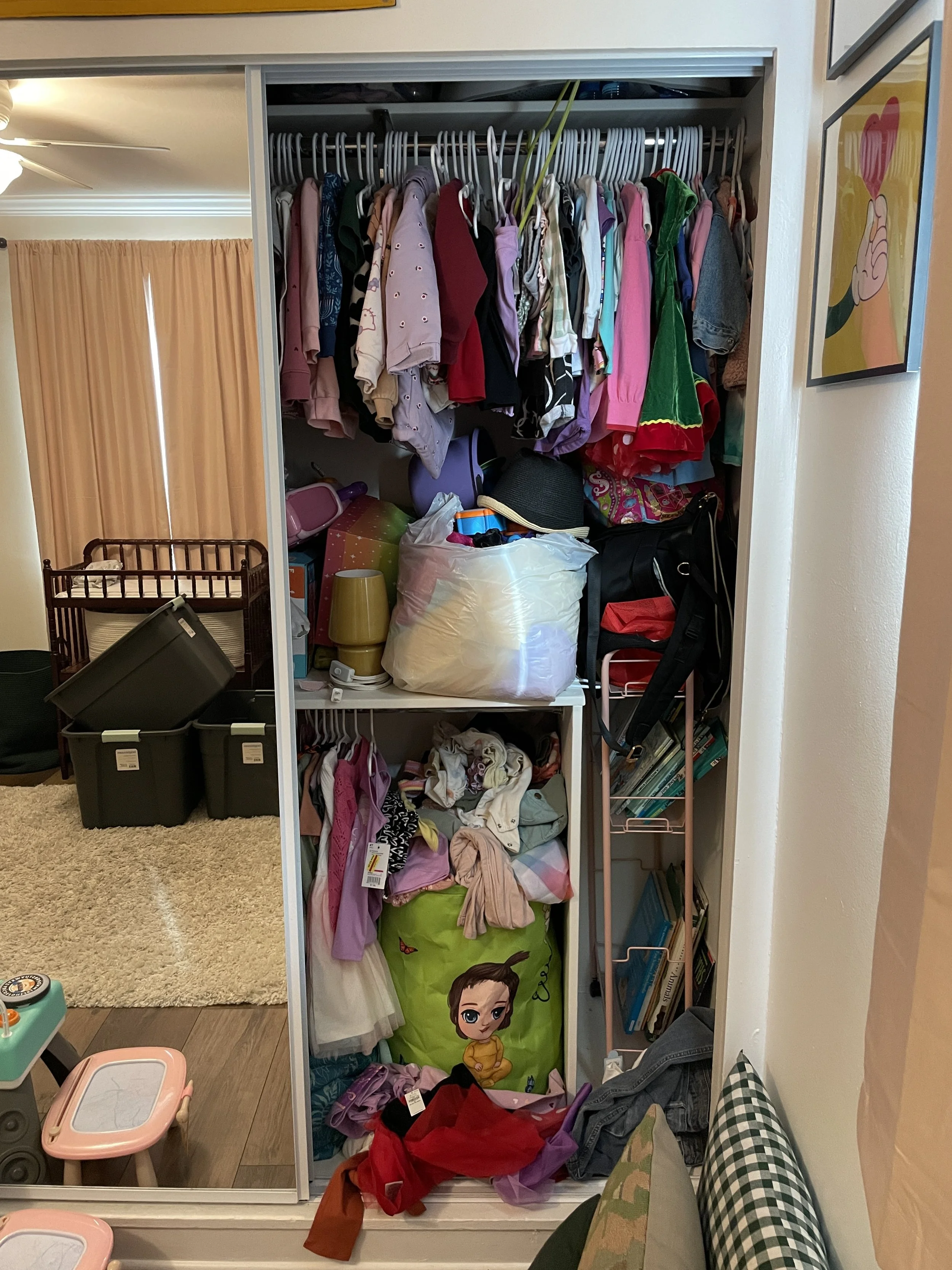 Open closet filled with hanging clothes, stored items, and storage bins. There are various clothes, a doll, and household items inside and around the closet.