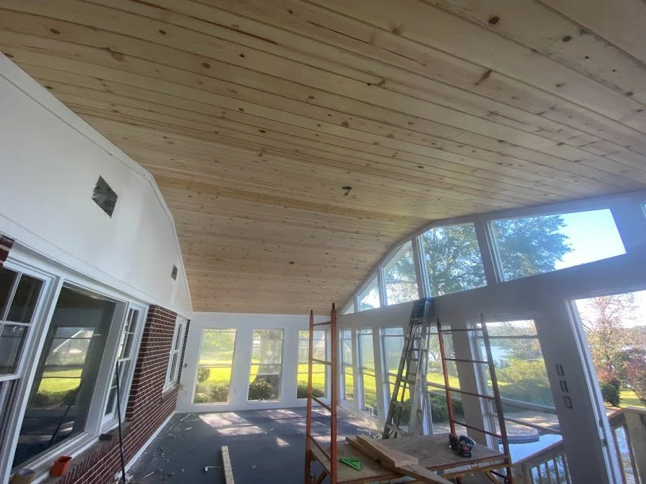 Interior of a house under construction with large windows, scaffolding, and a wooden ceiling.