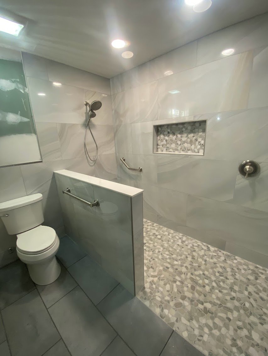 Custom walk-in tile shower with stone floor, waterproofing system, bench seating, and niche built by Saylor’s Home Services.