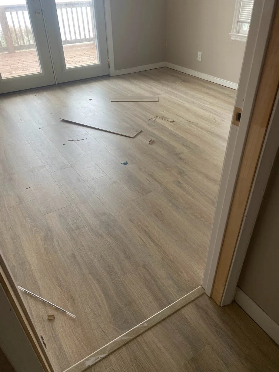 Room with new light wood flooring, debris, and plastic trim pieces on the floor, outside patio doors leading to a deck with a railing.