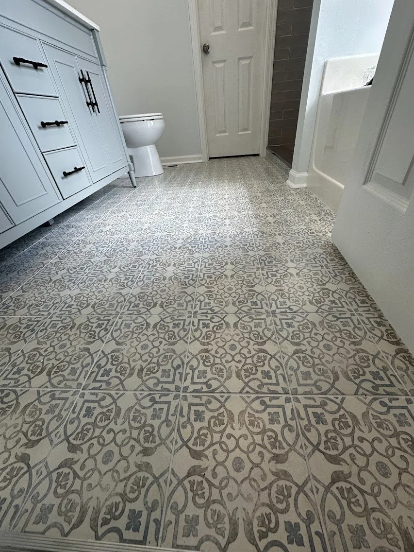Bathroom with patterned tile floor, white vanity, toilet, and partially visible shower area.