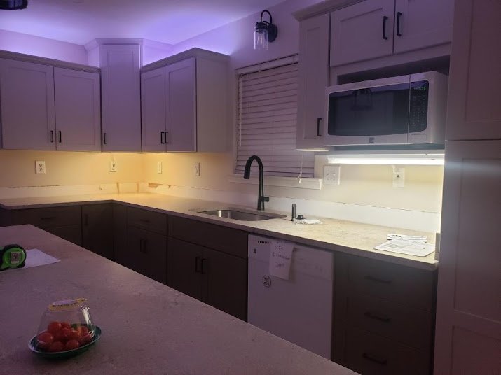 Kitchen with white cabinets, a black faucet, microwave, window with closed blinds, and a bowl of cherry tomatoes on the countertop.