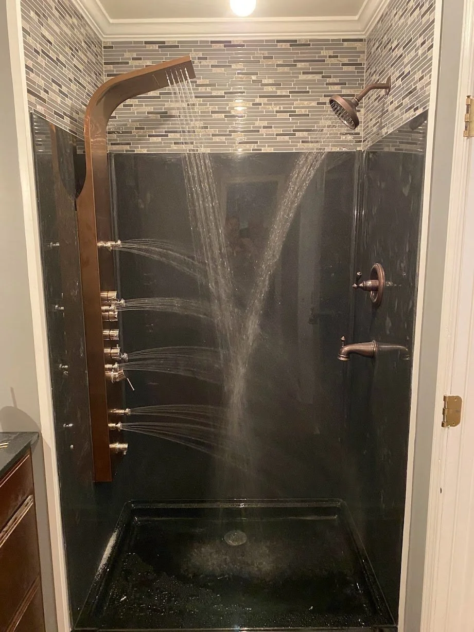 A shower with multiple water outlets, including a large overhead shower, a side showerhead, and several body jets on a wooden panel, within a tiled bathroom.